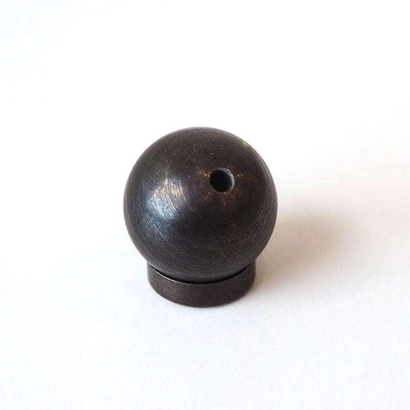 The Sphere Incense Holder is a small, dark brass sphere with a central hole, resting on a flat base against a plain white background, elegantly serving as a Japanese incense holder.