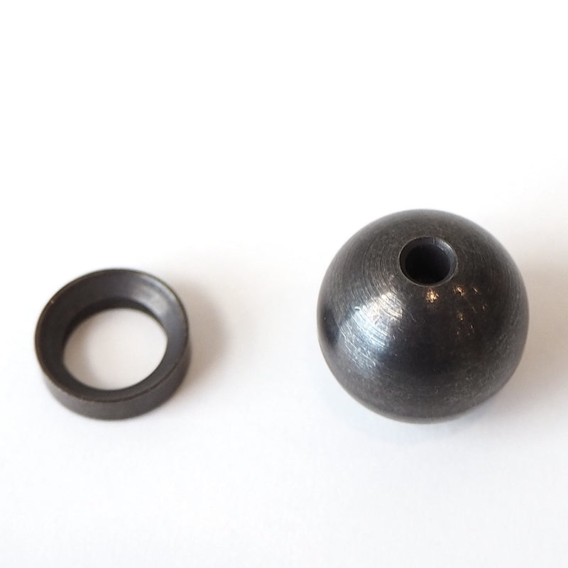 The Sphere Incense Holder, a brass metallic sphere with a small hole, is paired with an elegant flat ring and rests on a pristine white background.
