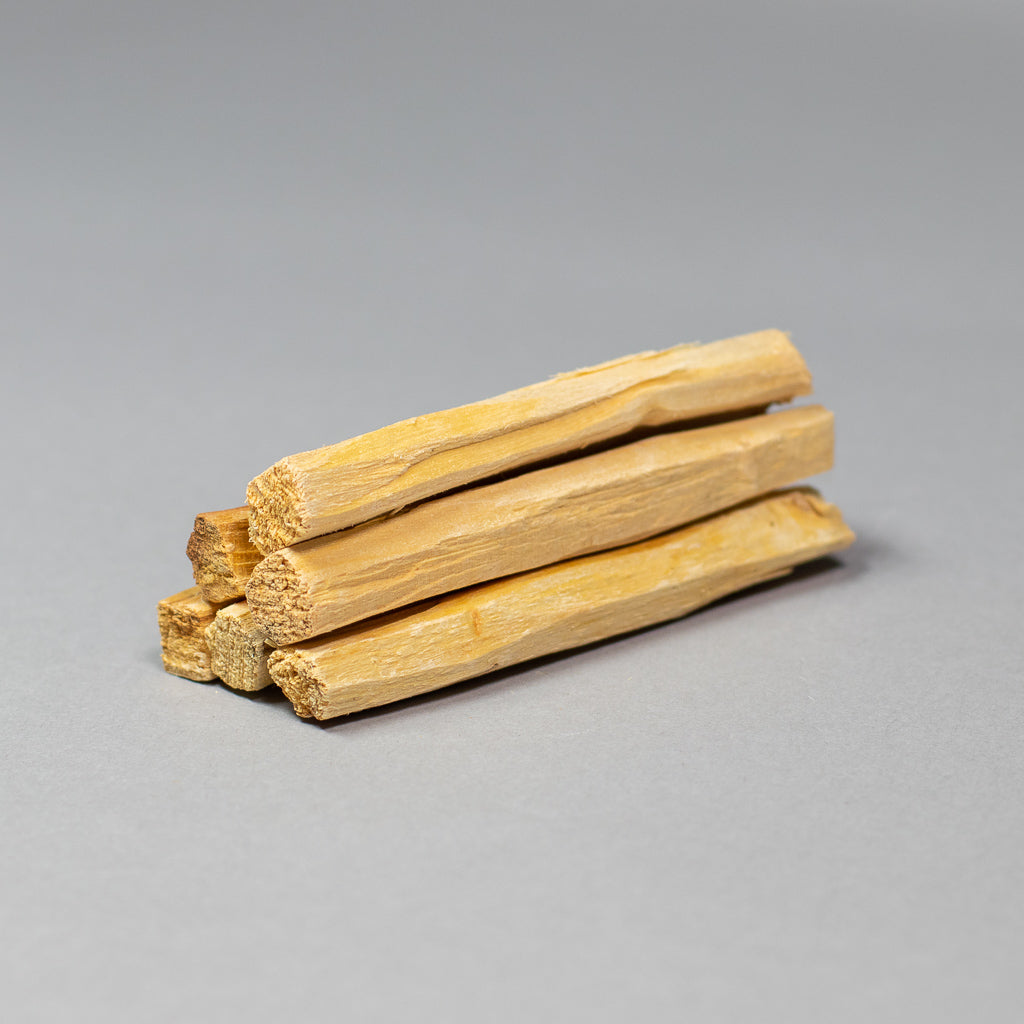 Four ethically harvested Palo Santo sticks from Ecuador, with a textured and fibrous appearance ideal for oral hygiene, are displayed on a gray background.