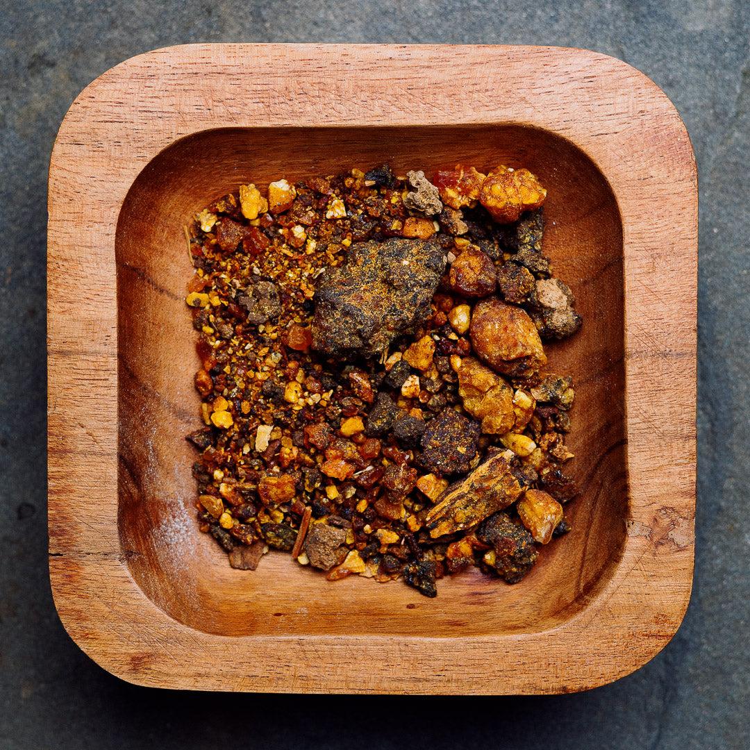 A rustic wooden bowl contains an assortment of earthy-toned Opoponax (Sweet Myrrh) Resin Incense pieces, showcasing shades of brown, orange, and yellow against a dark gray backdrop.