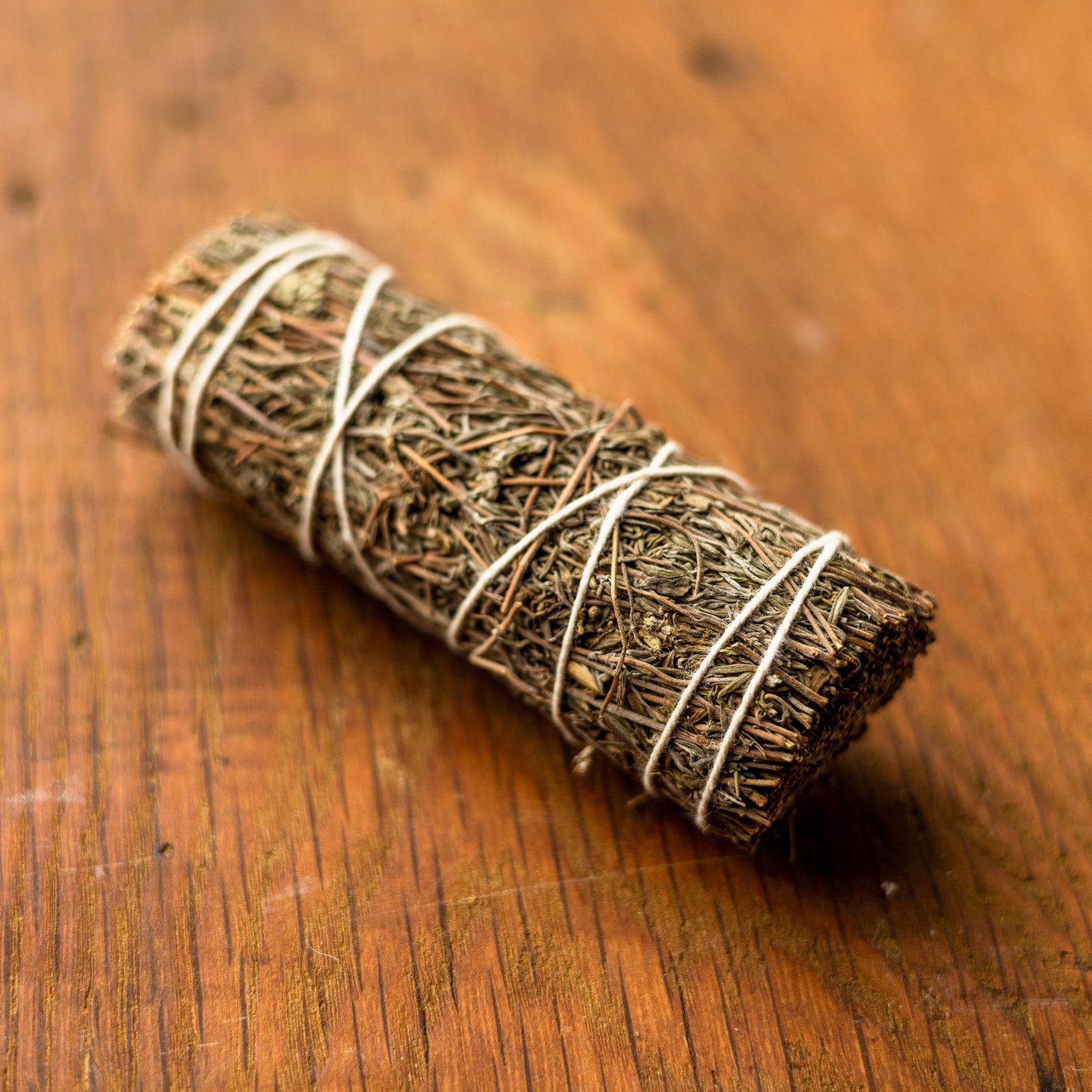 A Thyme Smudge Stick, tightly wrapped in white string, rests on a wooden surface.