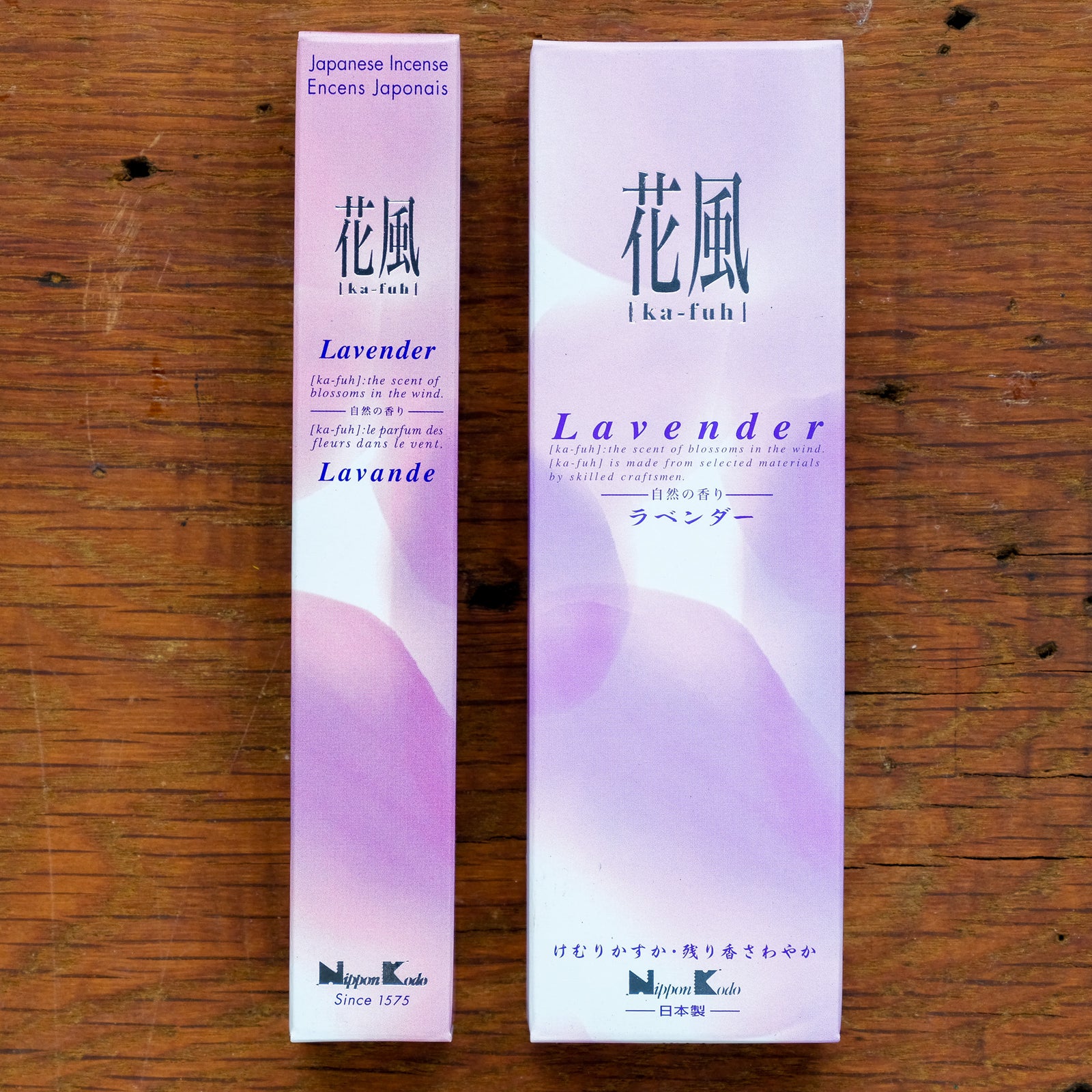 On a wooden surface are two boxes of Japanese-style incense. The larger box is Ka-Fuh Lavender Incense, labeled in English and Japanese. Both boxes have a soft purple and white gradient design, promising an authentic scent experience.