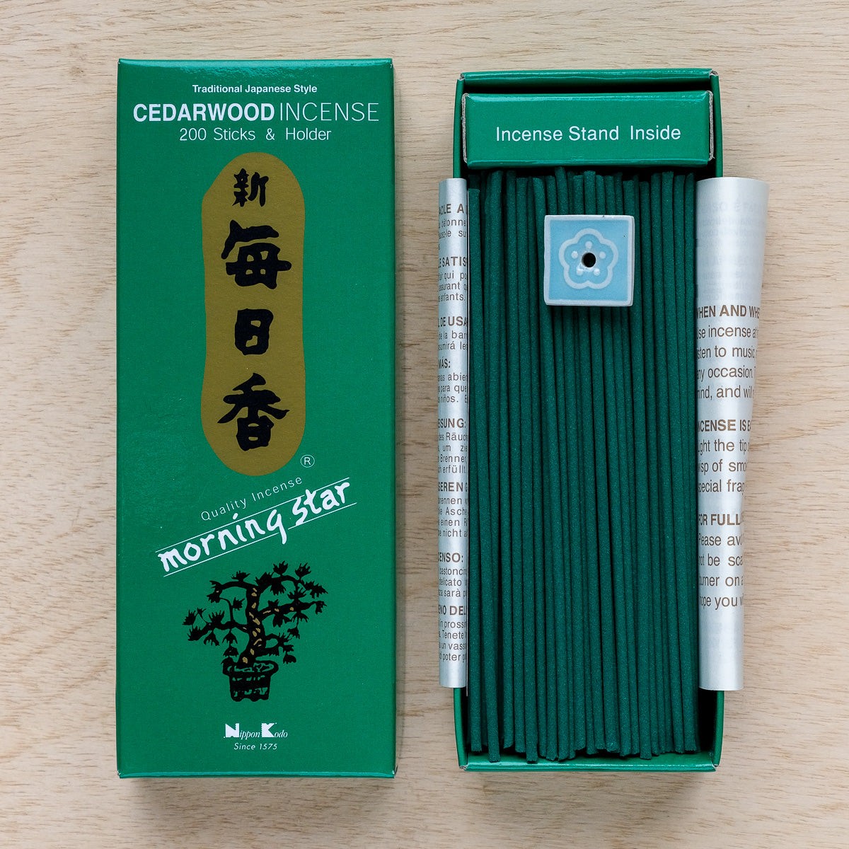 An open green box of Morning Star Cedarwood Incense reveals neatly stacked sticks ideal for meditation. The Japanese-style packaging includes elegant writing, product details on the inside flap, and a small ceramic holder.