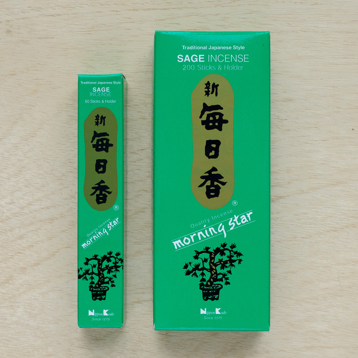Two green boxes of Morning Star Sage Incense are showcased on wood; the larger box, with a traditional Japanese style, holds 200 sticks and a holder, while the smaller one contains 50 sticks and a holder. Both exude the calming Sage fragrance.