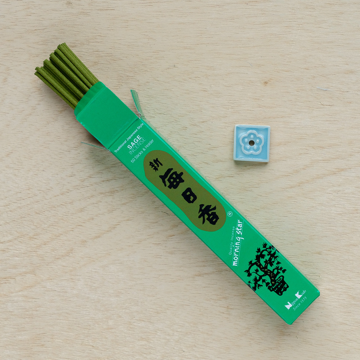 An open box of Morning Star Sage Incense in green rests on a wooden surface, accompanied by a small, square light blue incense holder featuring a floral design.