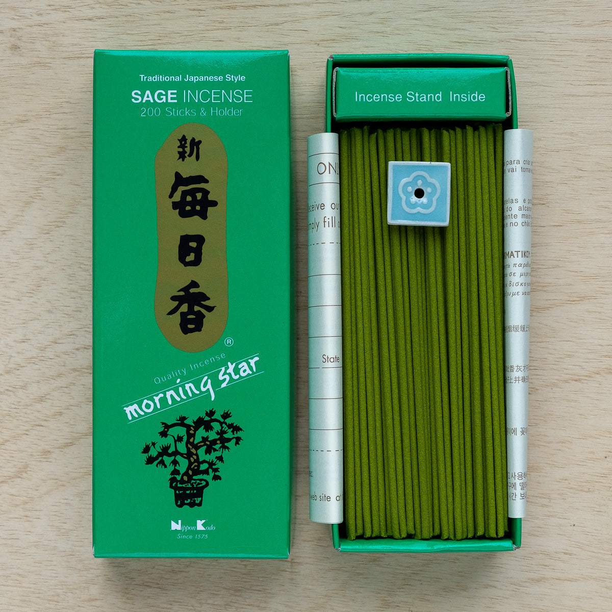 The Morning Star Sage Incense comes in a green box with 200 sticks and a blue flower-design holder. Featuring Japanese characters and a tree motif, the open package presents neatly arranged incense sticks, merging tradition with tranquility.