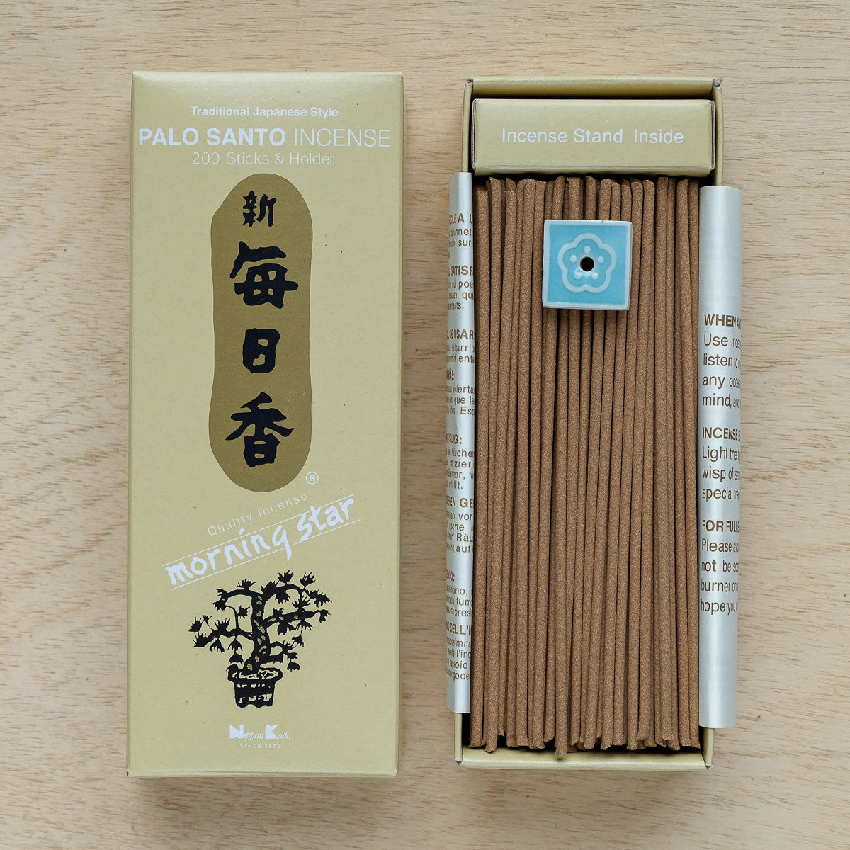 A box of Morning Star Palo Santo Incense contains 200 brown sticks with a hint of Frankincense and a small blue holder. The packaging, adorned with a tree design and Japanese characters, reveals neatly aligned sticks, embodying the essence of Japanese incense tradition.