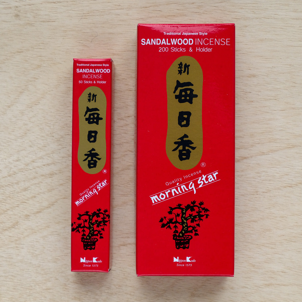 Two red boxes of Morning Star Sandalwood Incense provide a soothing sandalwood aroma. The larger box contains 200 sticks, and the smaller has 50. They feature Japanese characters, gold accents, and a tree image, elegantly resting on a light wood surface.