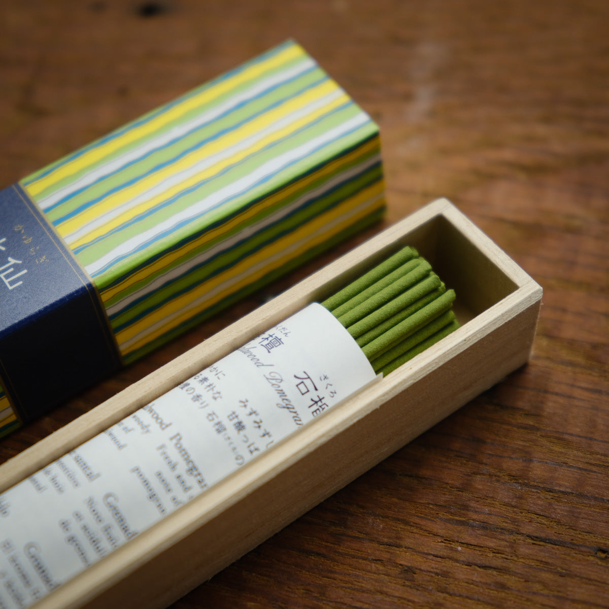 The Kayuragi Narcissus Incense, presented in a wooden box with a colorful striped lid and multilingual text inside, emits a soothing scented smoke, promising an aura of relaxation when placed on any wooden surface.