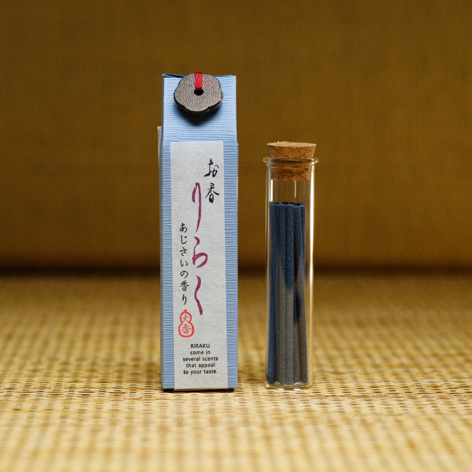 A light blue box labeled Riraku Hydrangea Incense from Japan and featuring washi paper with Japanese text rests beside a small cork-capped glass vial filled with black incense sticks crafted by Nippon Kodo.