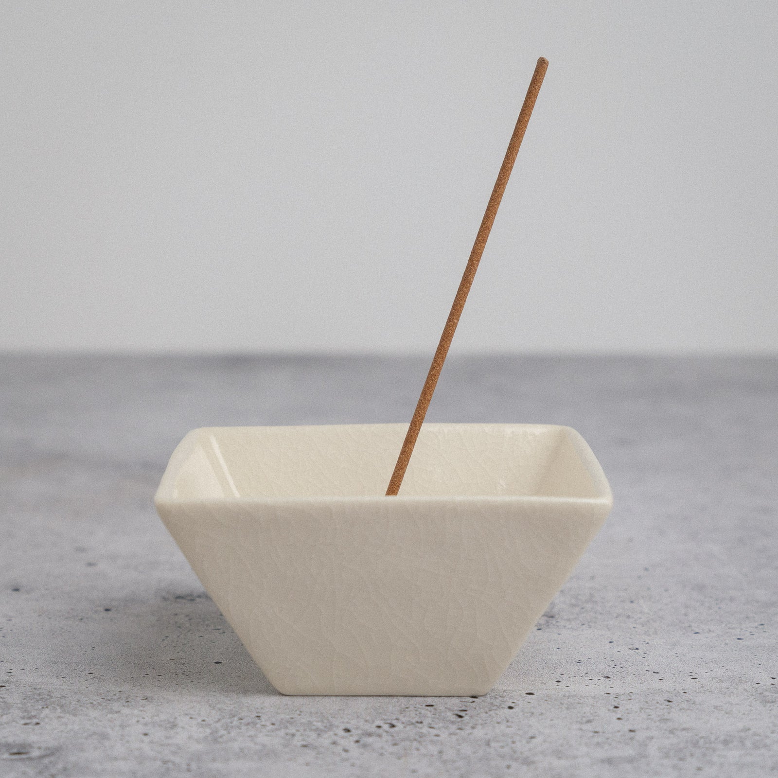 Beige ceramic incense holder with a single incense stick on a gray surface