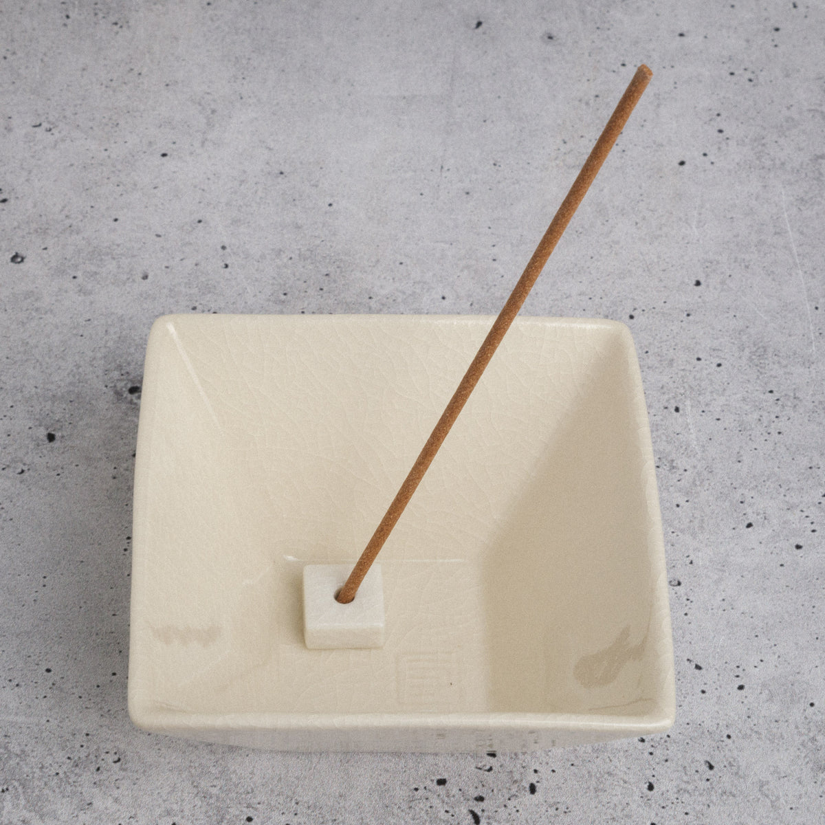 Rectangular white incense burner with a wooden incense stick on a gray speckled surface