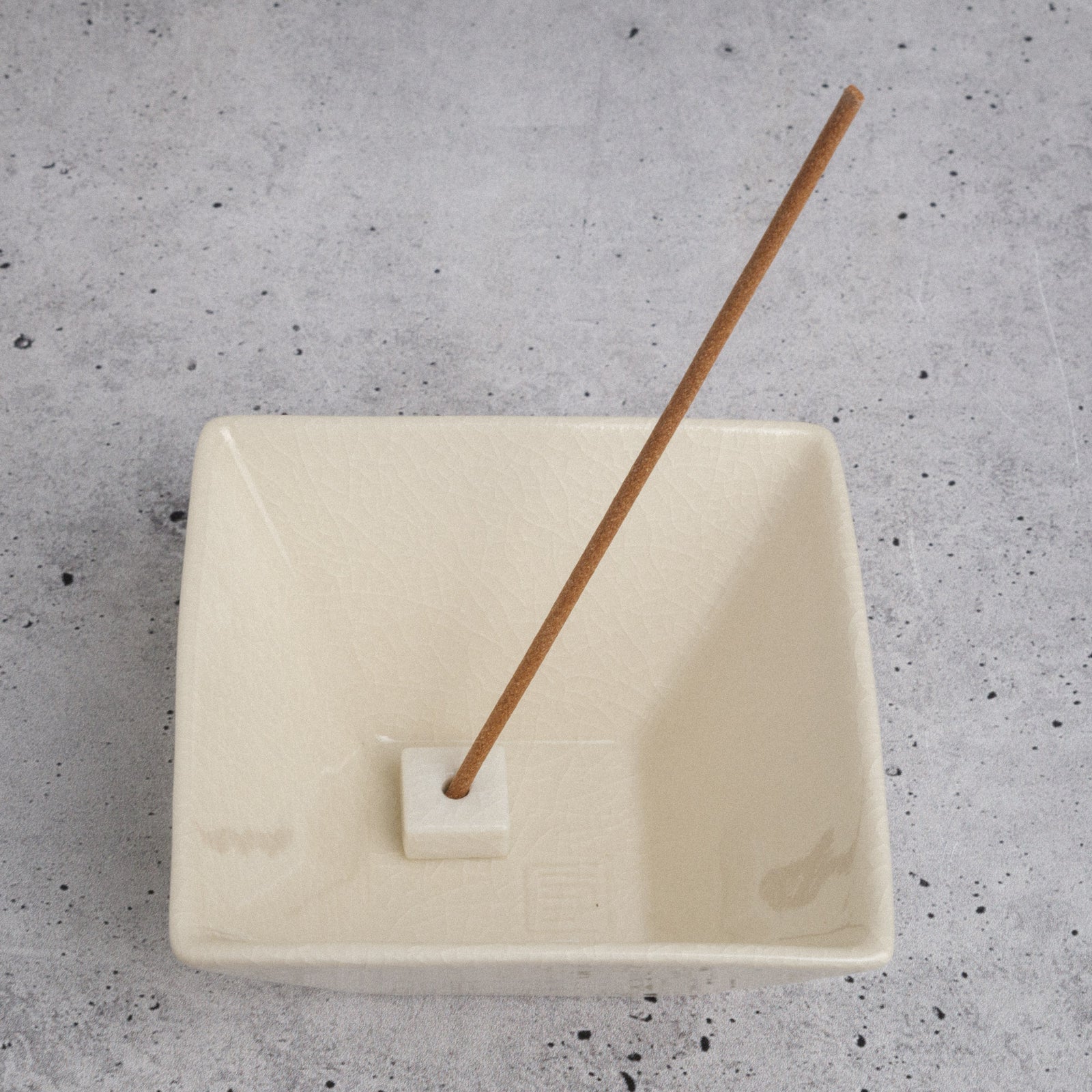 Rectangular white incense burner with a wooden incense stick on a gray speckled surface