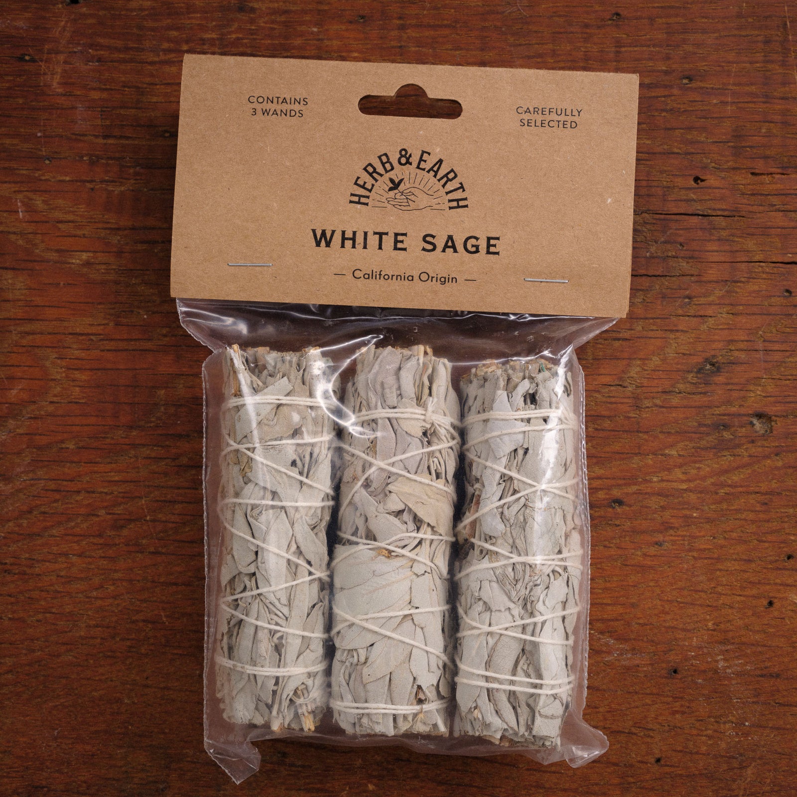 Packaged white sage sticks with a 'Herb & Earth' label on a wooden surface