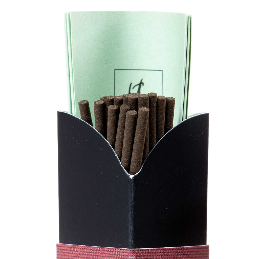 An open black box of Jinkoh Juzan Aloeswood Japanese Incense with a maroon base band displays densely packed brown sticks and a partially visible folded green paper behind them.