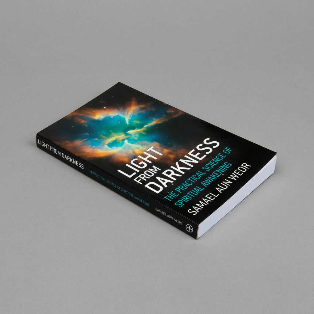 The 2012 edition of Light from Darkness by Samael Aun Weor, a paperback book, lies on a gray surface. Its cover displays a cosmic scene symbolizing spiritual awakening, with light emerging from darkness.