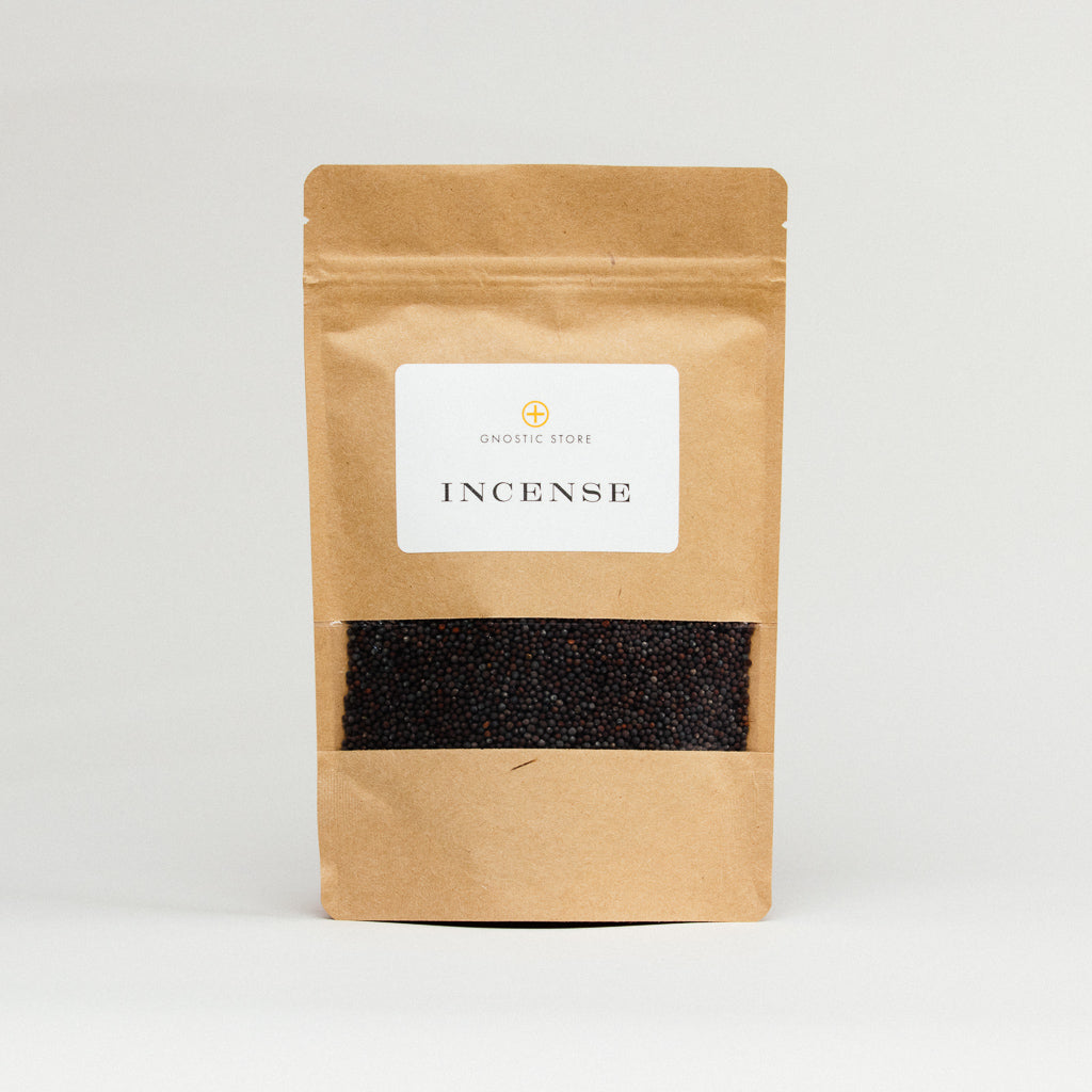 The brown paper bag, showcasing the Onostic Store logo, displays Black Mustard Seeds, Organic through a clear window. The small dark granules resemble black mustard seeds, projecting an aura of psychic protection as it stands upright on a plain light background.