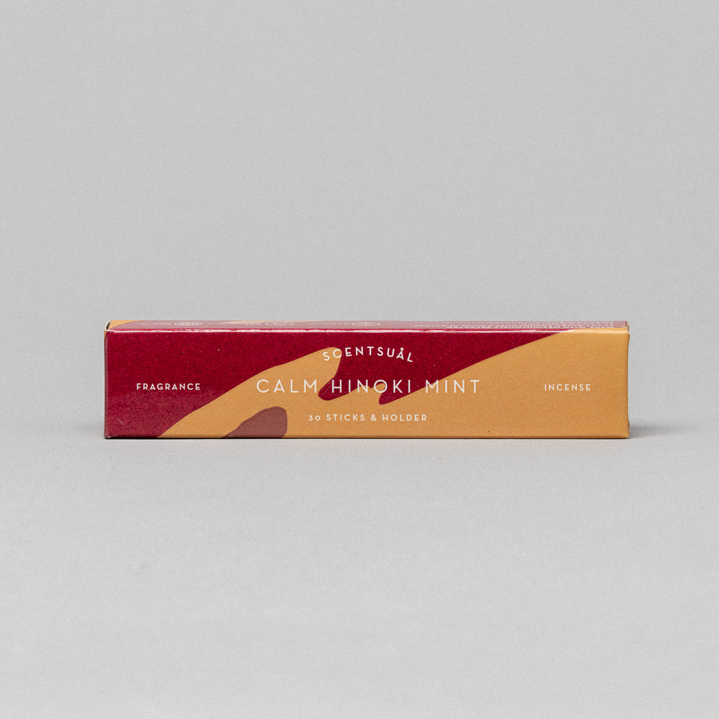 The Scentsual Japanese Incense box offers the refreshing scent of Calm Hinoki Mint. Its minimalist red, orange, and beige packaging includes 30 sticks and a holder, all set against a simple gray background.