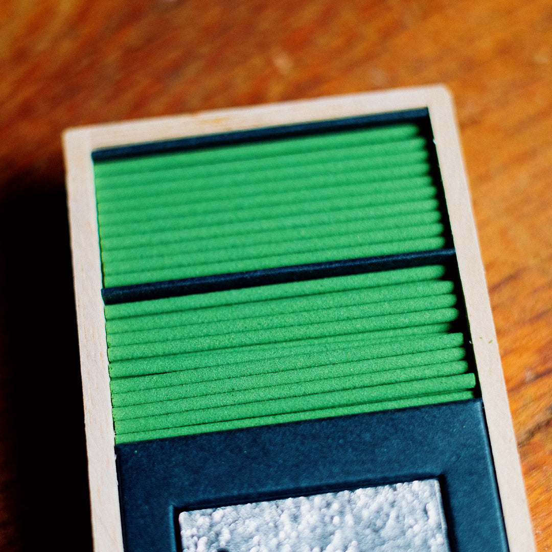 A close-up of the Oedo-Koh Pine Tree Incense shows green sticks neatly arranged in a gift box with a white border and a small silver section, set on a wooden surface.