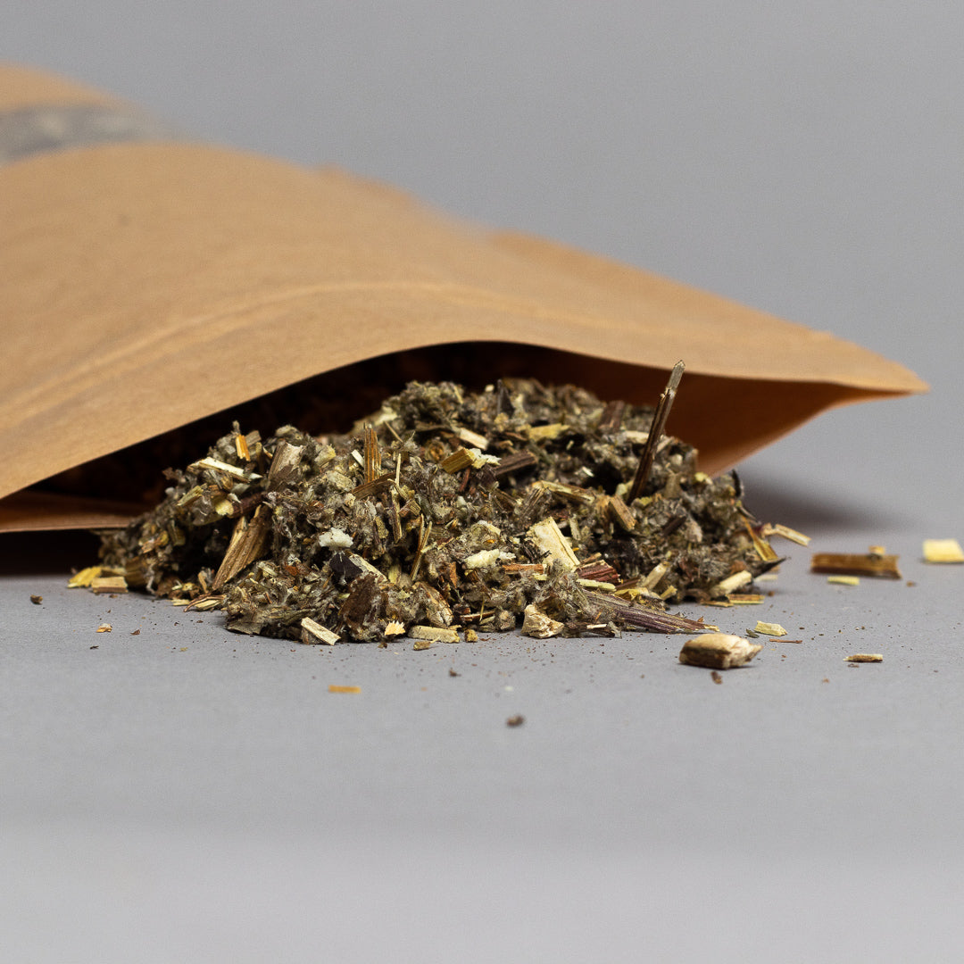 A bag labeled Black Sage (Mugwort) Loose spills a mix of dried herbs onto a gray surface, displaying varying shades of green and brown. The neutral background highlights the blend.