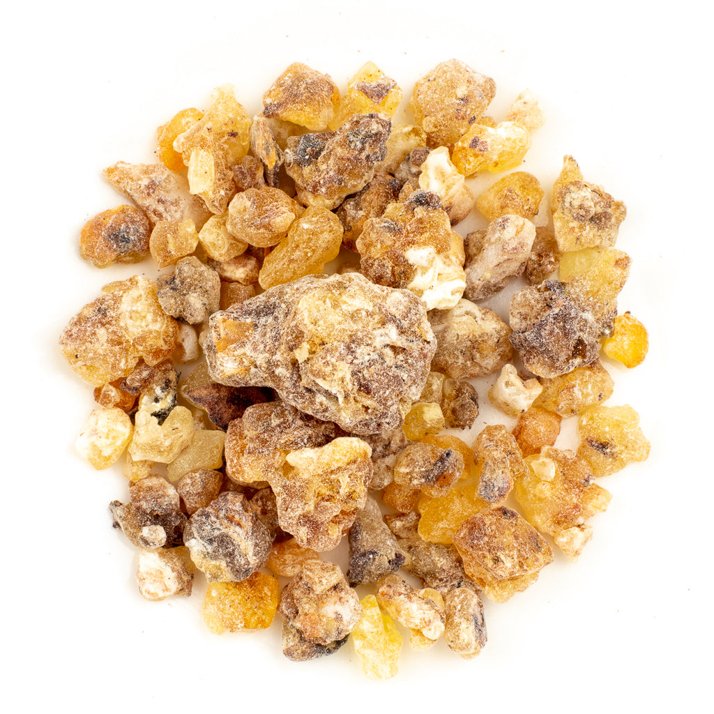 A close-up of a pile of Frankincense Resin Incense: First Grade Maydi (organic Boswellia frereana from Somalia) reveals small, irregular amber granules on a white background; some are darker and rough, others lighter and smooth, with an overall crystalline appearance and varied sizes.