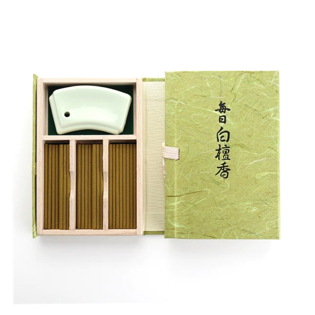 The open box reveals a Mainichi Byakudan Premium Sandalwood Japanese Incense set, showcasing a light green ceramic holder and brown incense sticks in wooden compartments. The green box, adorned with Japanese text, suggests traditional sandalwood essence for meditation fragrance.
